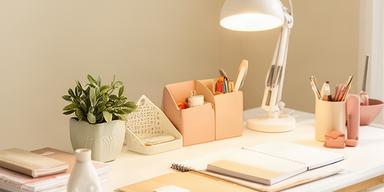 Escritorio de home office con lámpara de escritorio, planta pequeña y organizador decorativo en ambiente luminoso